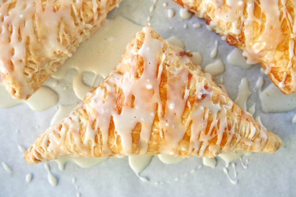 close up of the glaze on vegan apple turnovers on white parchment paper