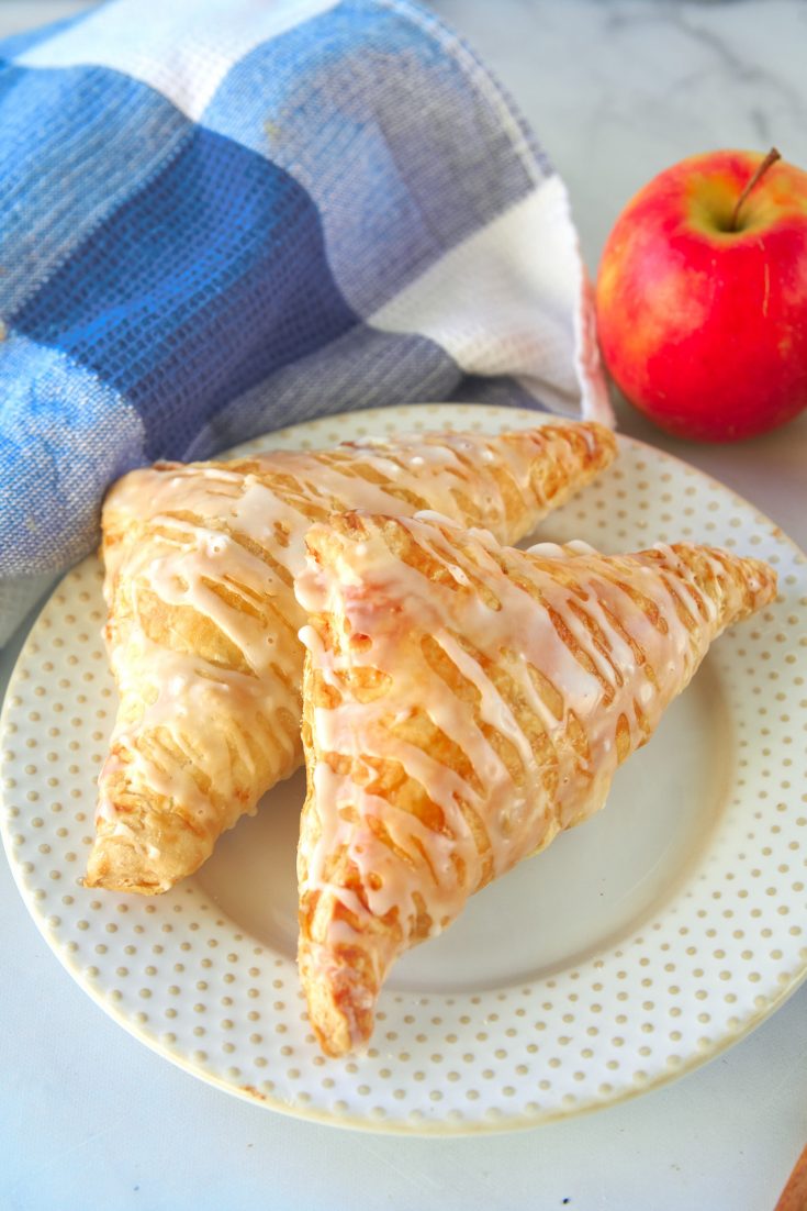 two vegan apple turnovers on a plate with an apple in the background