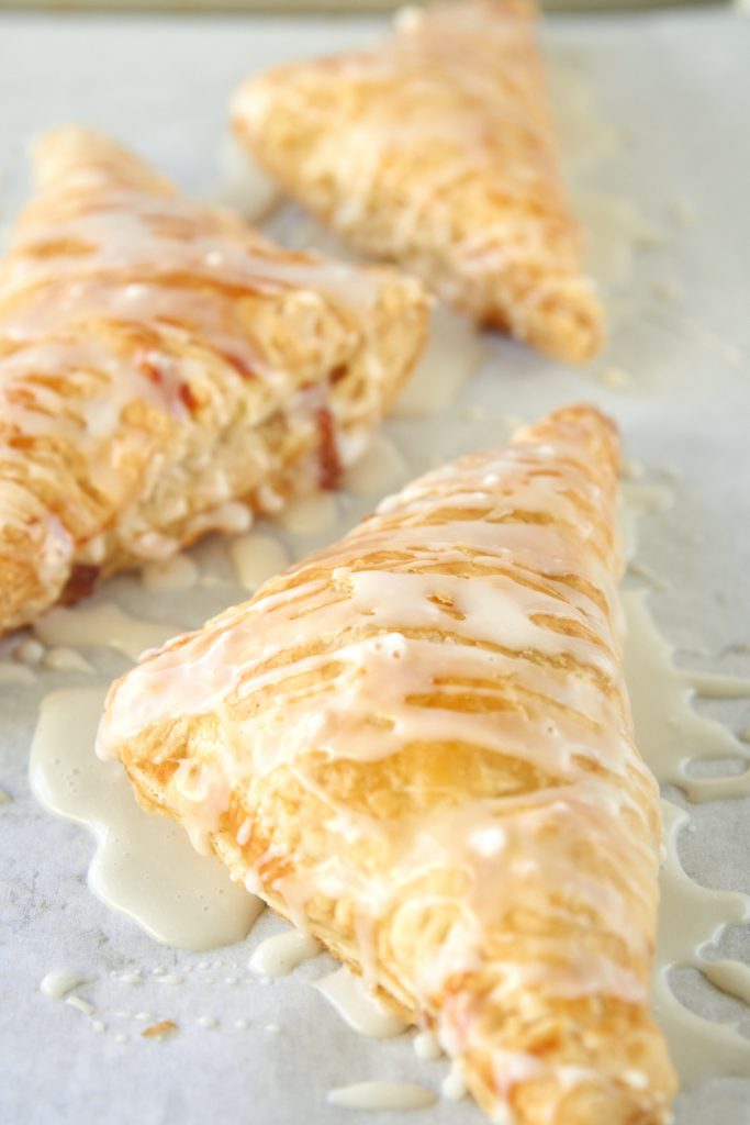 close up of a brown apple turnover with vegan glaze on it on parchment paper