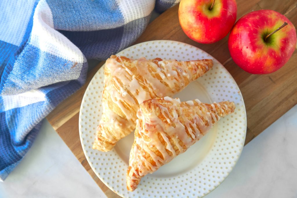 two vegan apple turnovers on plate with apples and dish towel