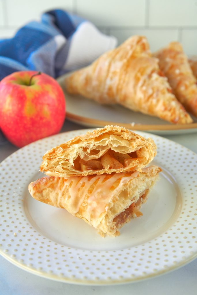 vegan apple turnover cut in half so you can see the inside with other turnovers and a red apple in the background
