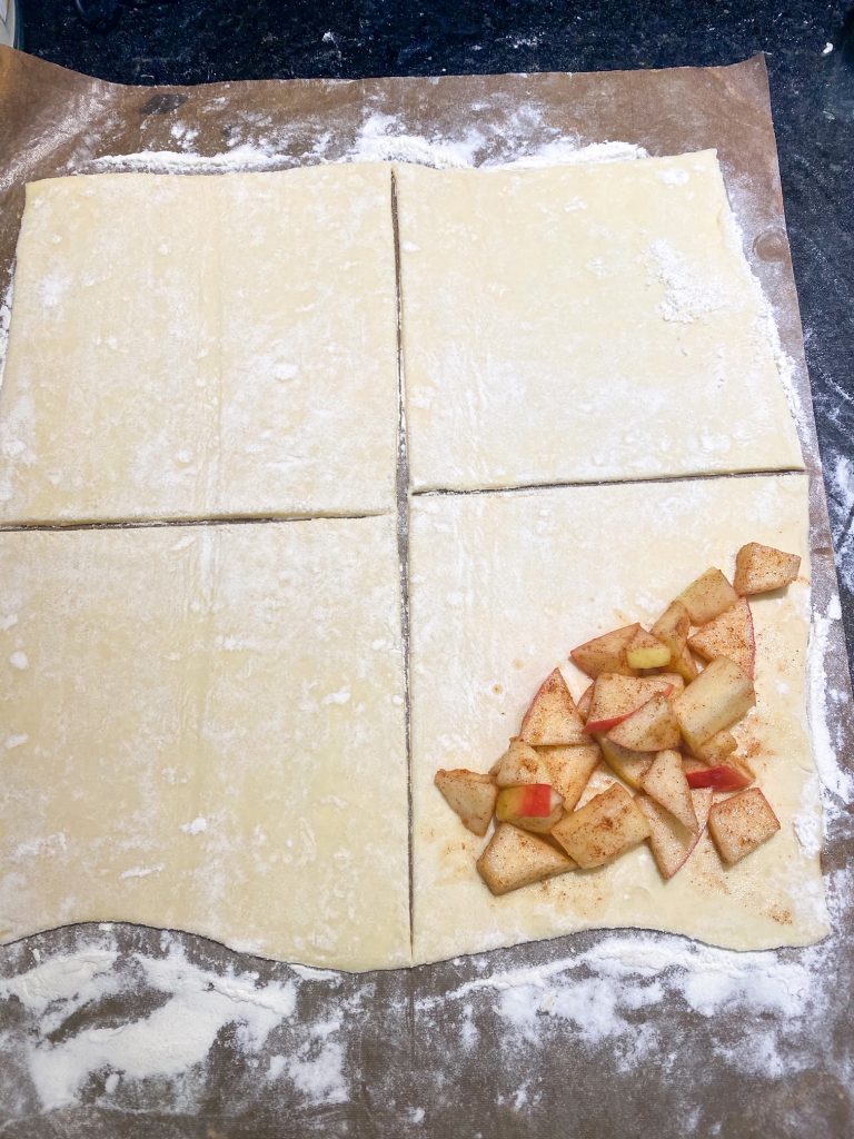 tan puff pastry cut into four squares with apples on the bottom right square