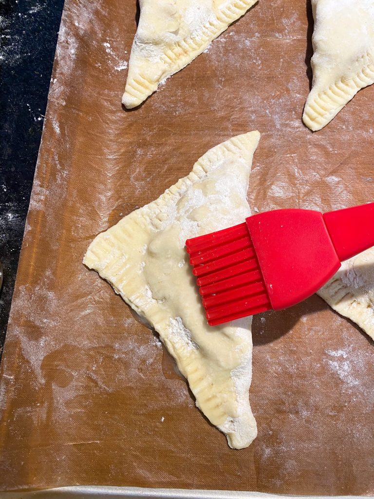 red brush painting on vegan egg wash to a triangle shaped dough turnover