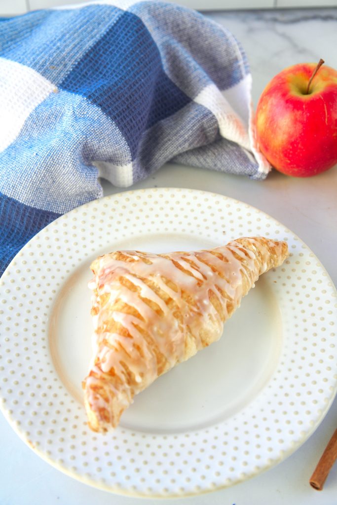 one healthy apple turnover on a serving plate with blue towel in the background and red apple