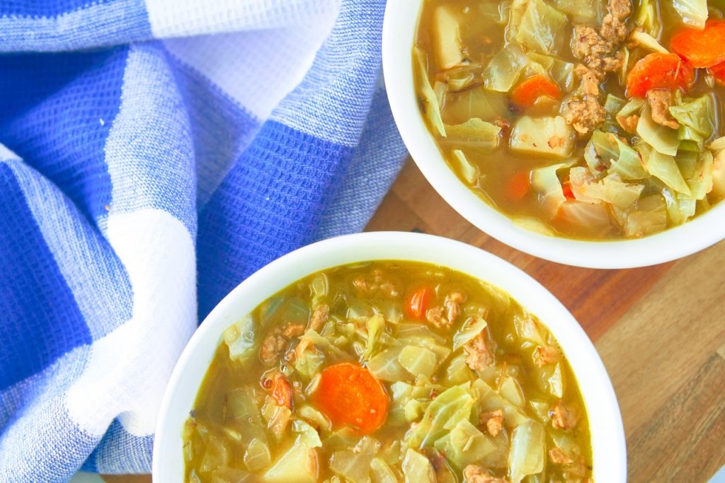 Straight down photo of two bowls of vegan cabbage soup on serving tray with blue and white towel.