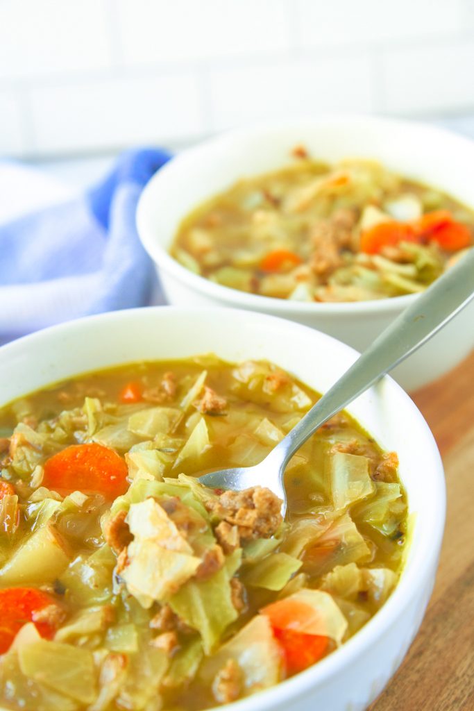 A spoon scooping up a bite of vegetarian cabbage soup with another bowl in the background.