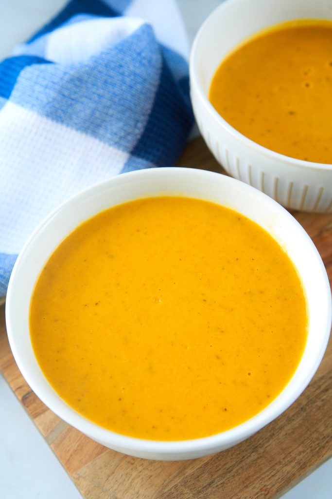 Plain vegan carrot soup in two white bowls with a blue towel.