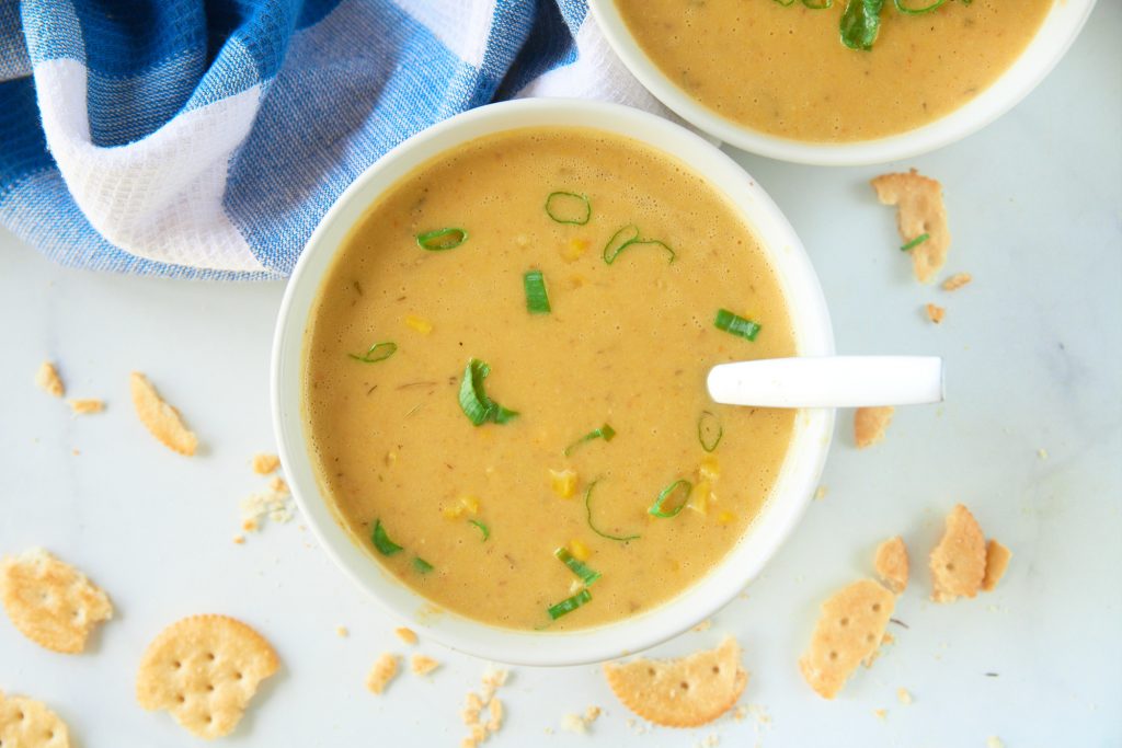 Two white bowls of corn chowder from above with crackers scattered around.