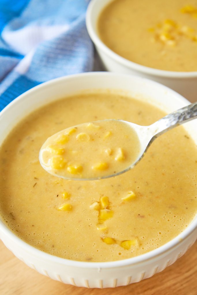 A spoon scooping up thick vegan corn chowder from a white bowl.