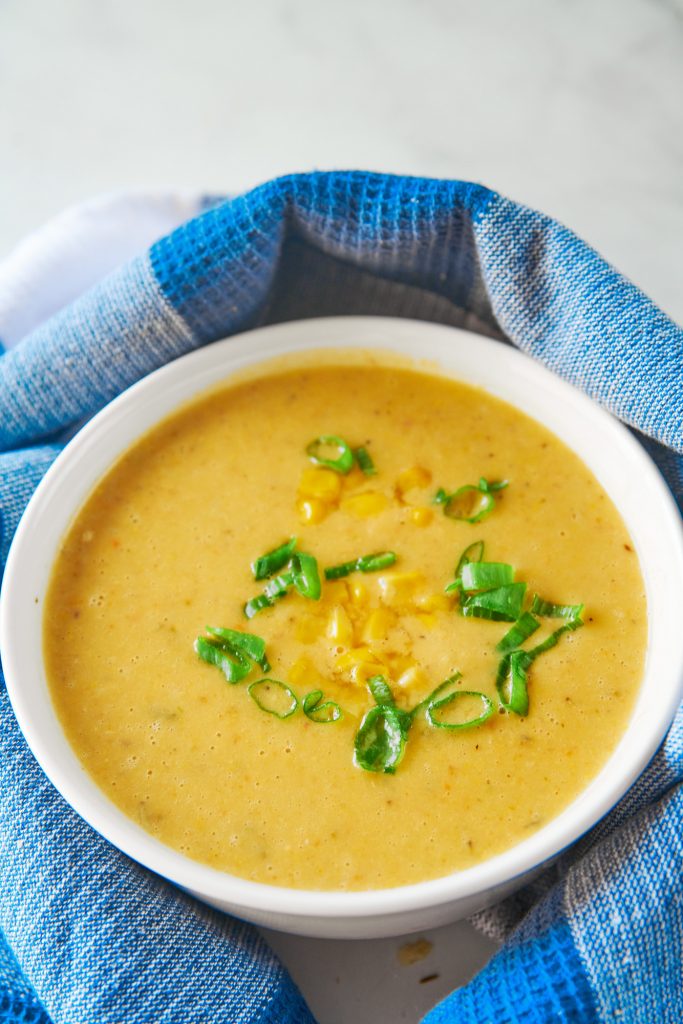 A close up of yellow corn soup with corn and green onions in a white bowl on 