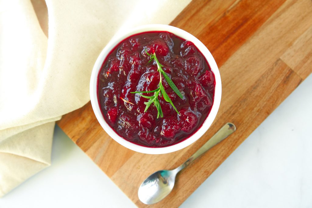 small spoon on the side of red cranberries in a bowl with green rosemary on top of them