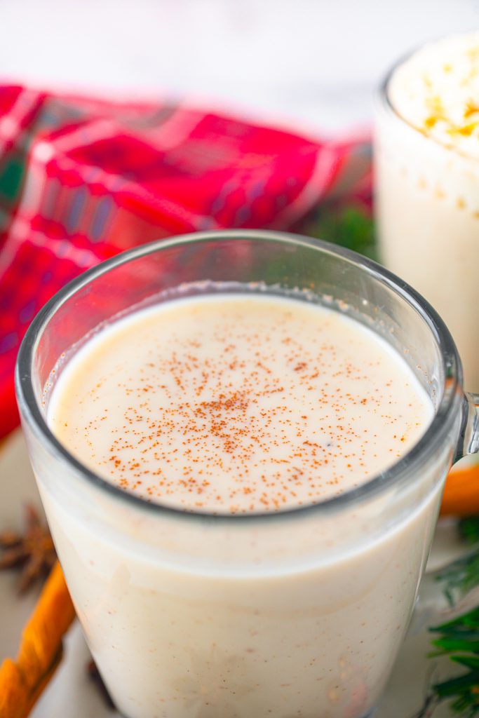 close up of white color eggless eggnog in a chilled serving glass with cinnamon on top of it 