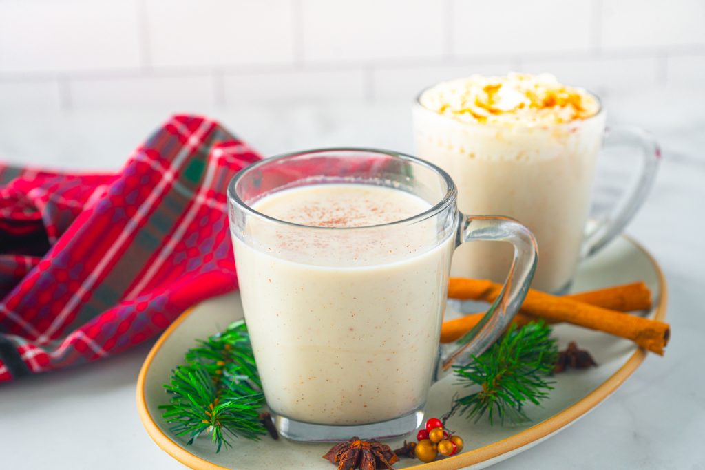 two cups of non-dairy eggnog with christmas decorations and a red plaid towel