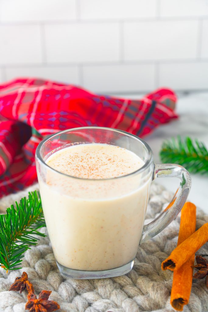 vegan eggnog recipe in a serving glass with cinnamon on the table with red tartan plaid in the background 
