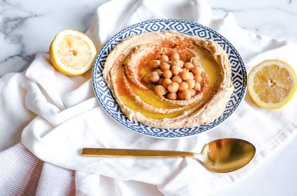 vegan hummus in a plate with spoon and lemons for serving