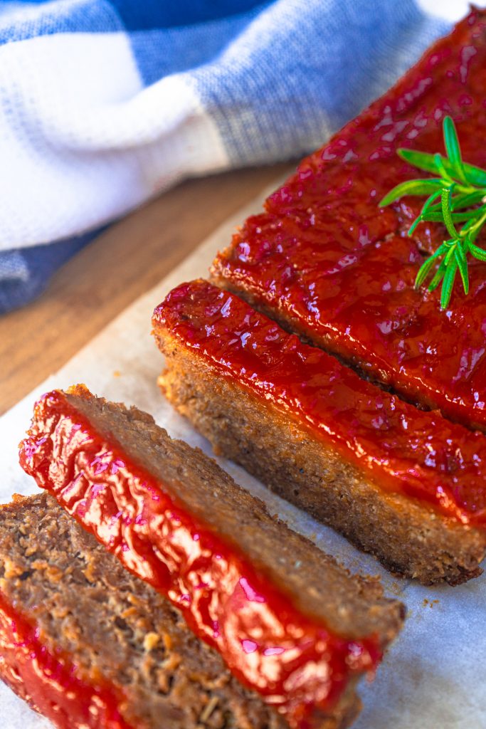 vegan meatloaf with red ketchup glaze cut into slices with rosemary garnish