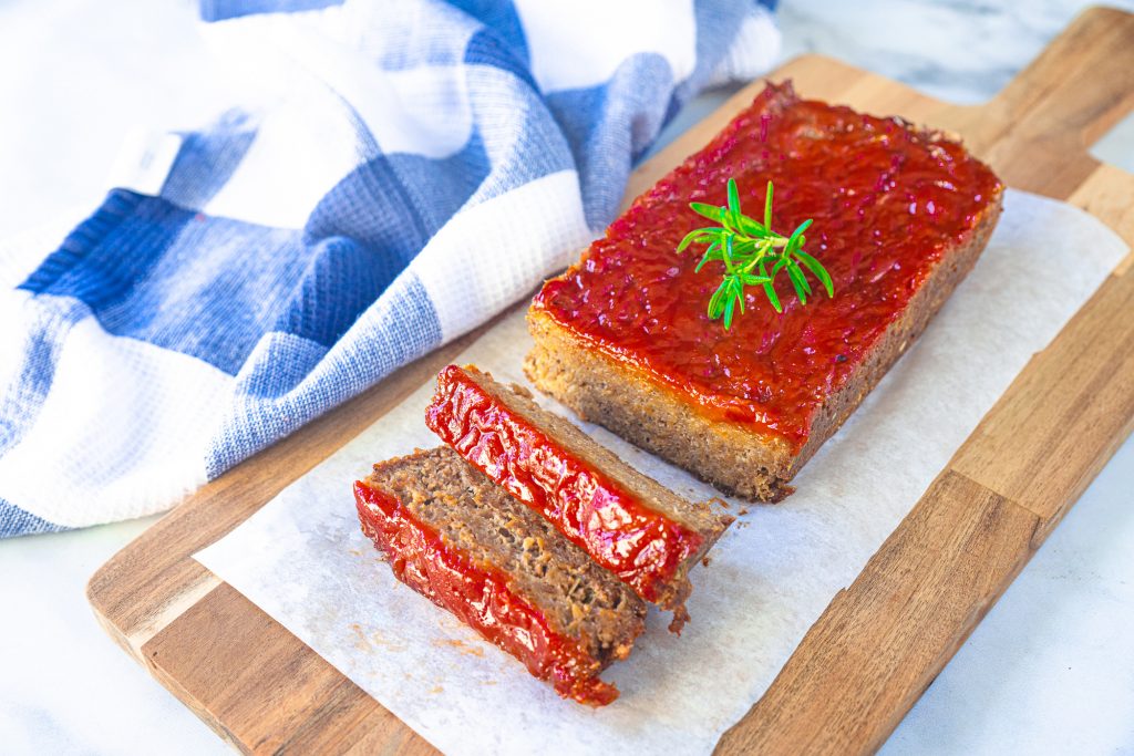 vegan meatloaf recipe with red ketchup glaze on top, sliced and on breadboard for serving
