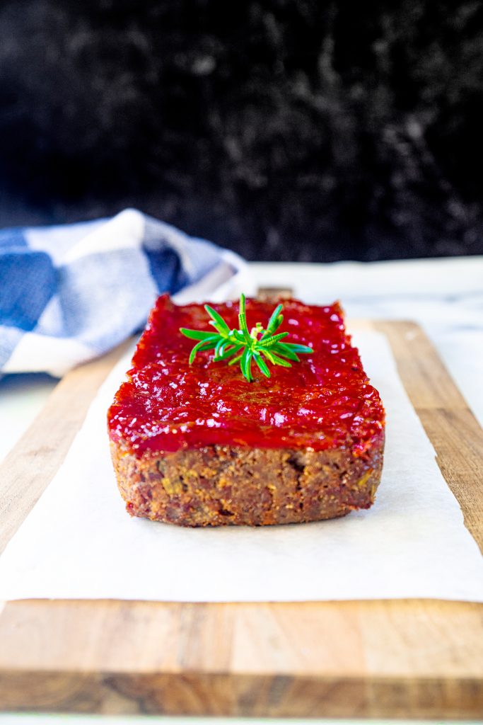 vegetarian meatloaf on serving tray on top of a white piece of parchment with black background and blue towel