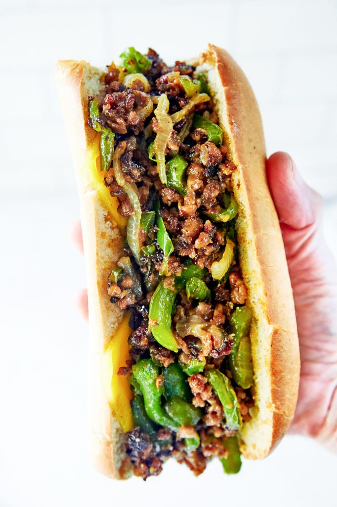 hand holding a vegan philly cheesesteak sandwich