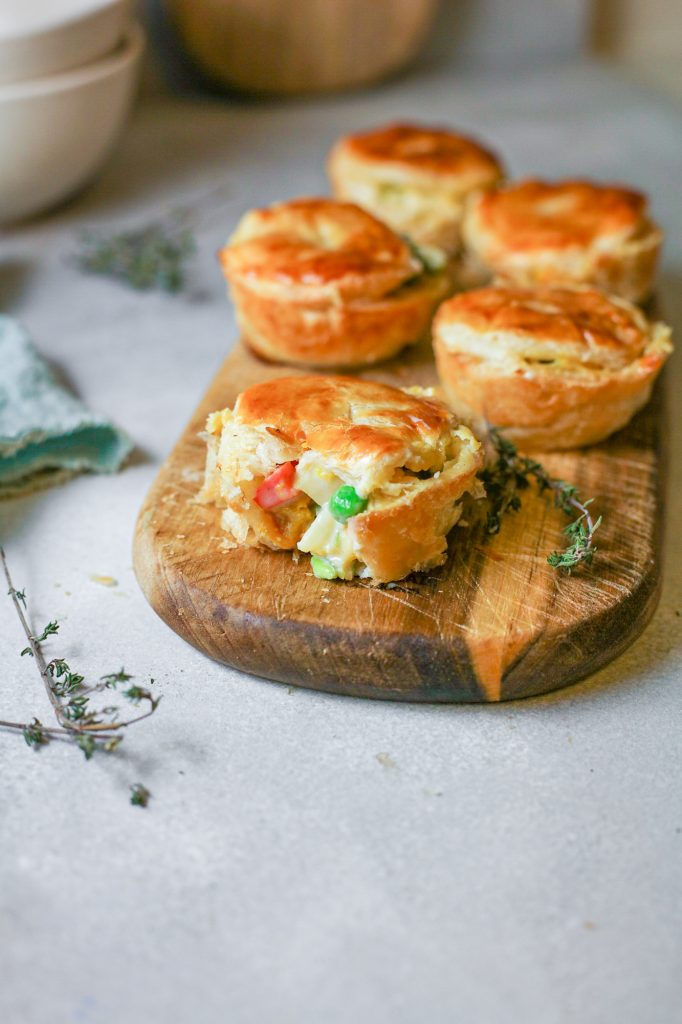 Row of mini vegan pot pies on a wooden serving tray with one cut open.