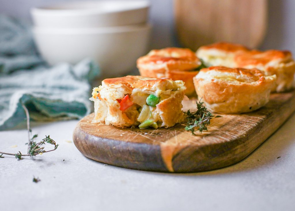 A cut piece of vegan vegetable pot pie with filling spilling out next to more on a wooden tray.