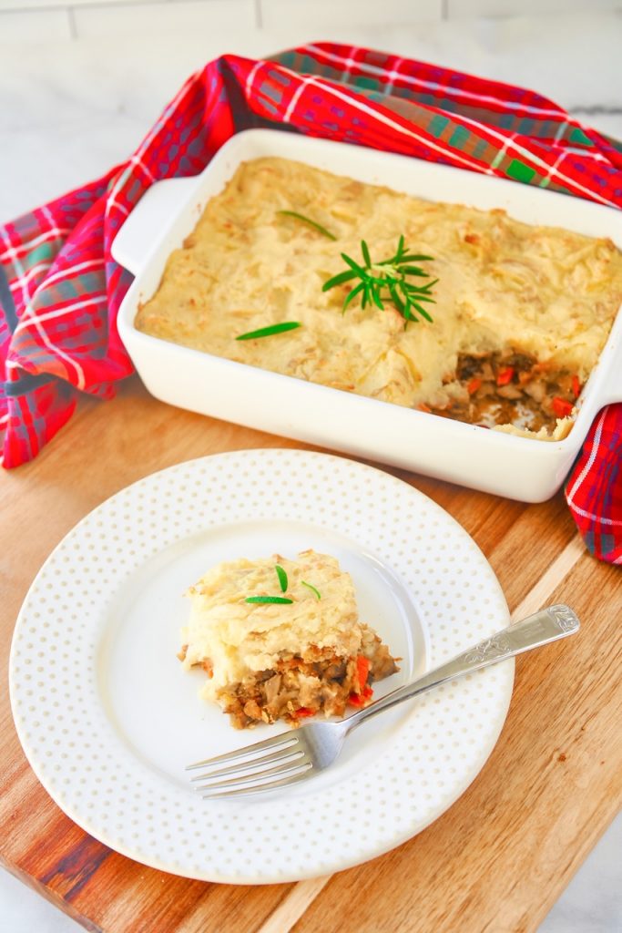 A slice of vegan lentil shepherd's pie on a white plate on a counter next to a casserole.