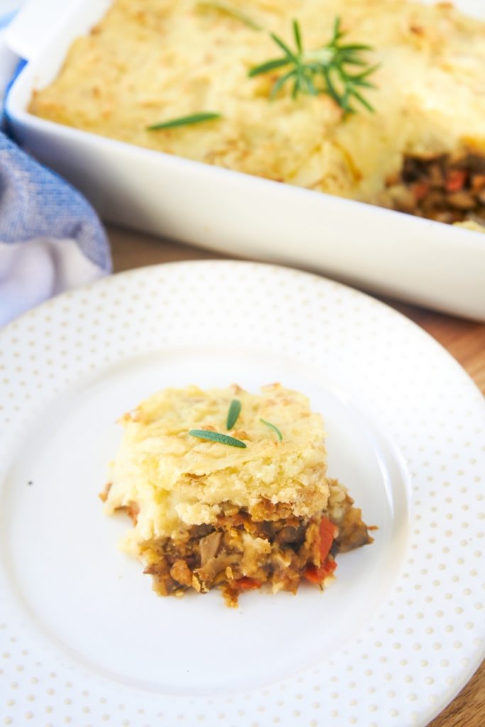 A close up of a slice of vegan cottage pie with lentils on white plate.