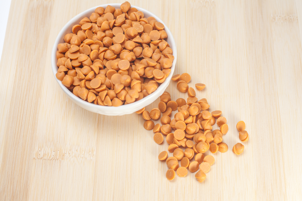 butterscotch morsels in a white bowl on a brown, wood counter