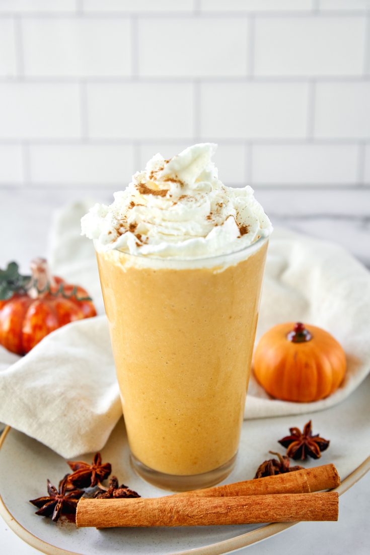 vegan pumpkin spice frappuccino in a tall glass with whipped cream and cinnamon