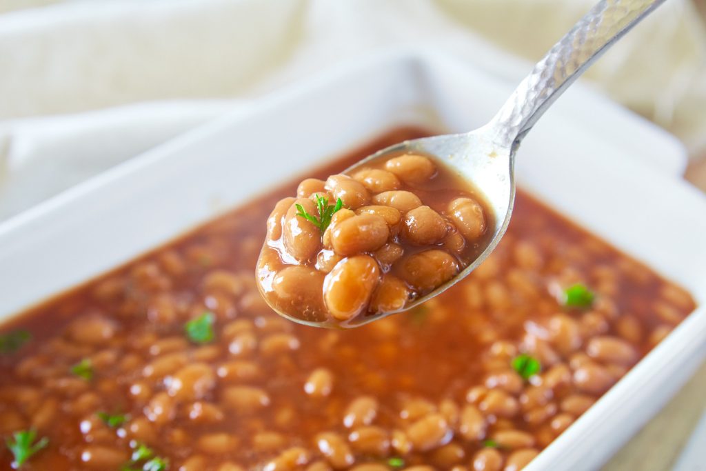 spoon scooping up homemade vegan baked beans out of a casserole dish