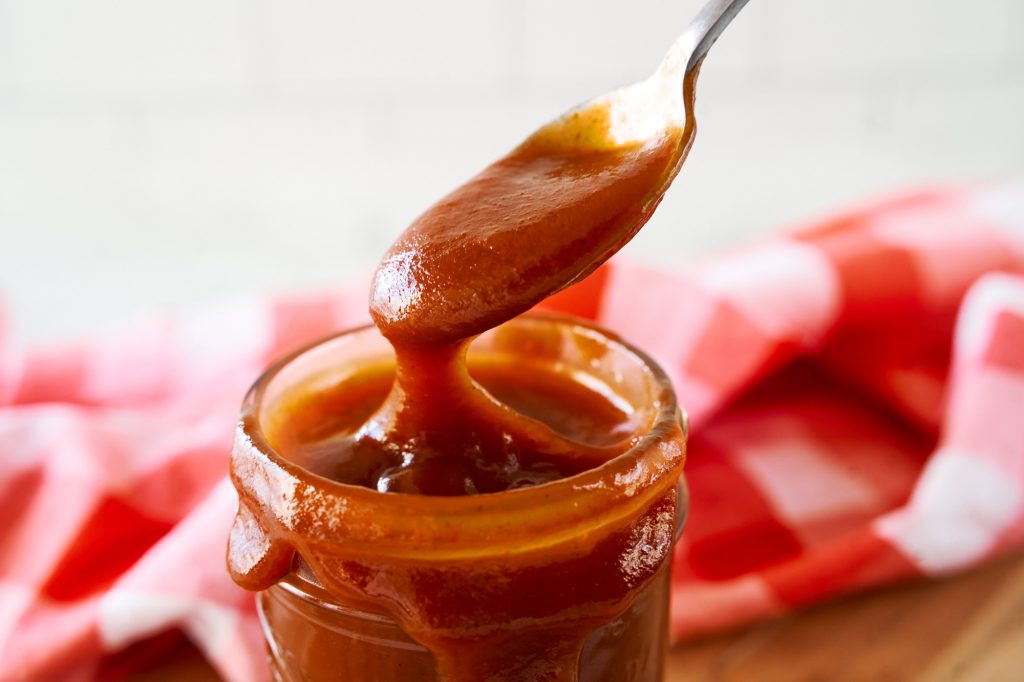 close up on a spoon scooping up vegan bbq sauce from a jar