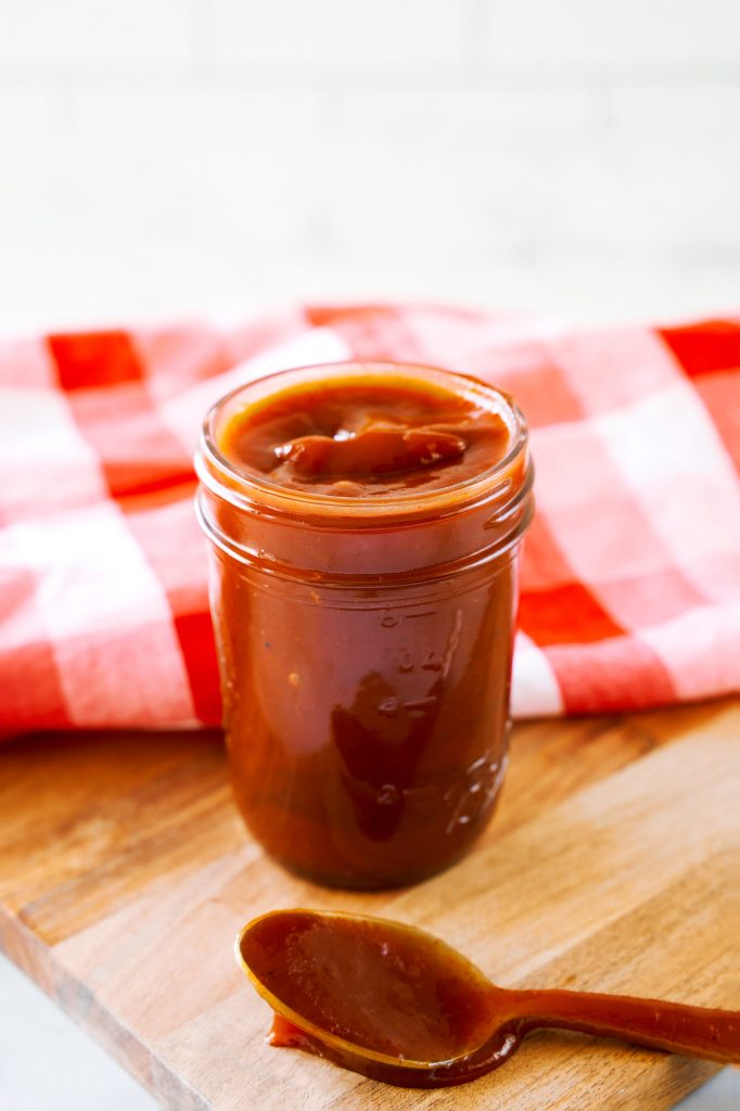 spoon filled with vegan barbecue sauce on bread board with container in the back