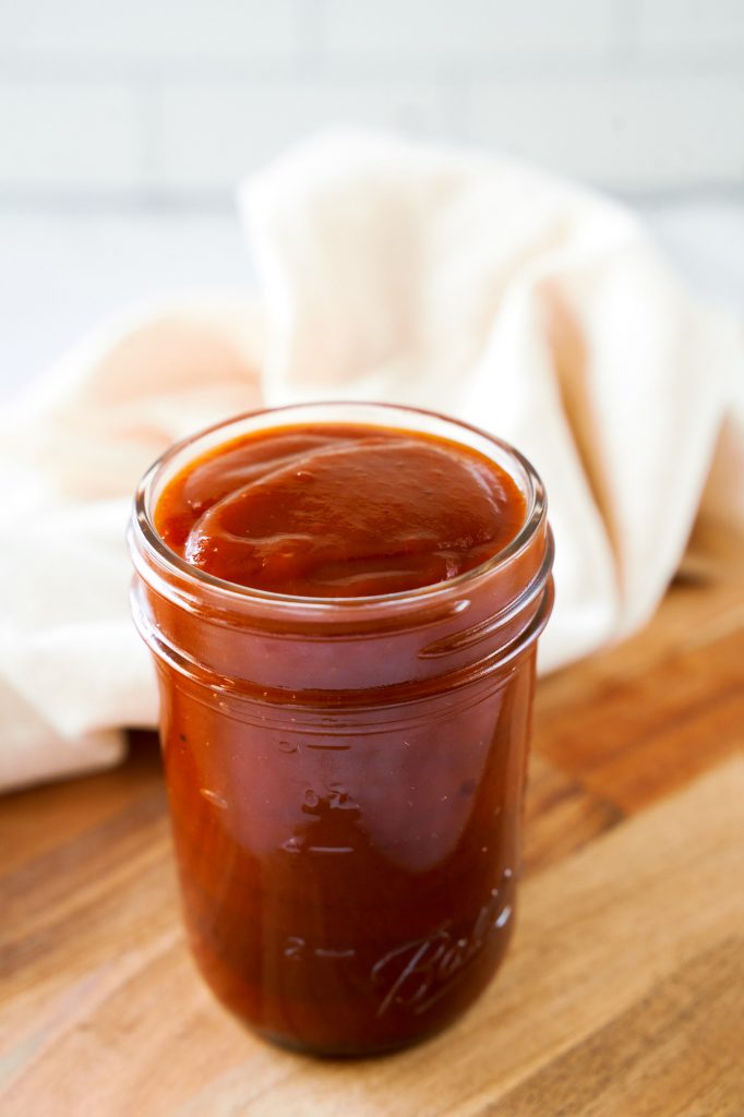 close up of homemade vegan barbecue sauce in a jar with a tan towel