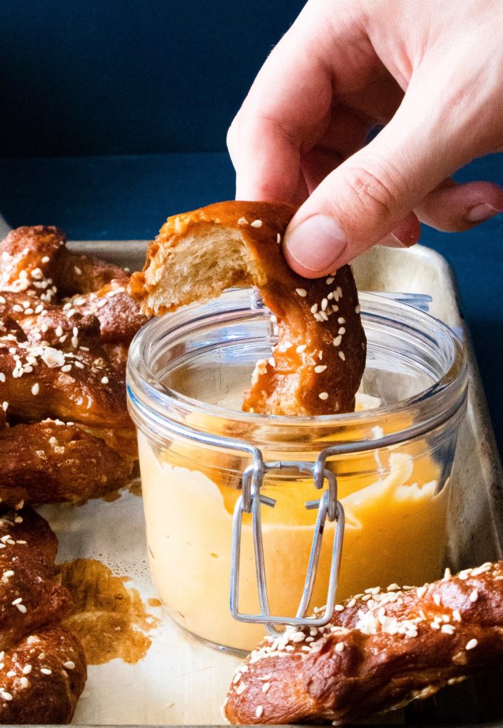 dipping a piece of pretzel into vegan beer cheese dip