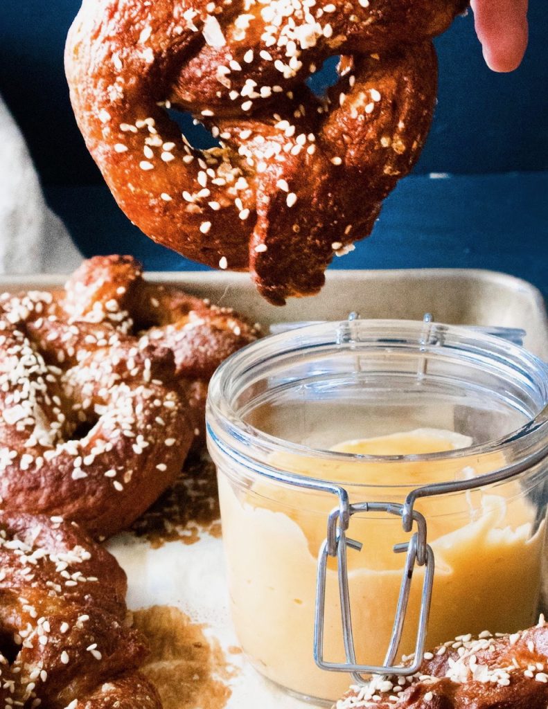 dipping large pretzel into vegan beer cheese dip