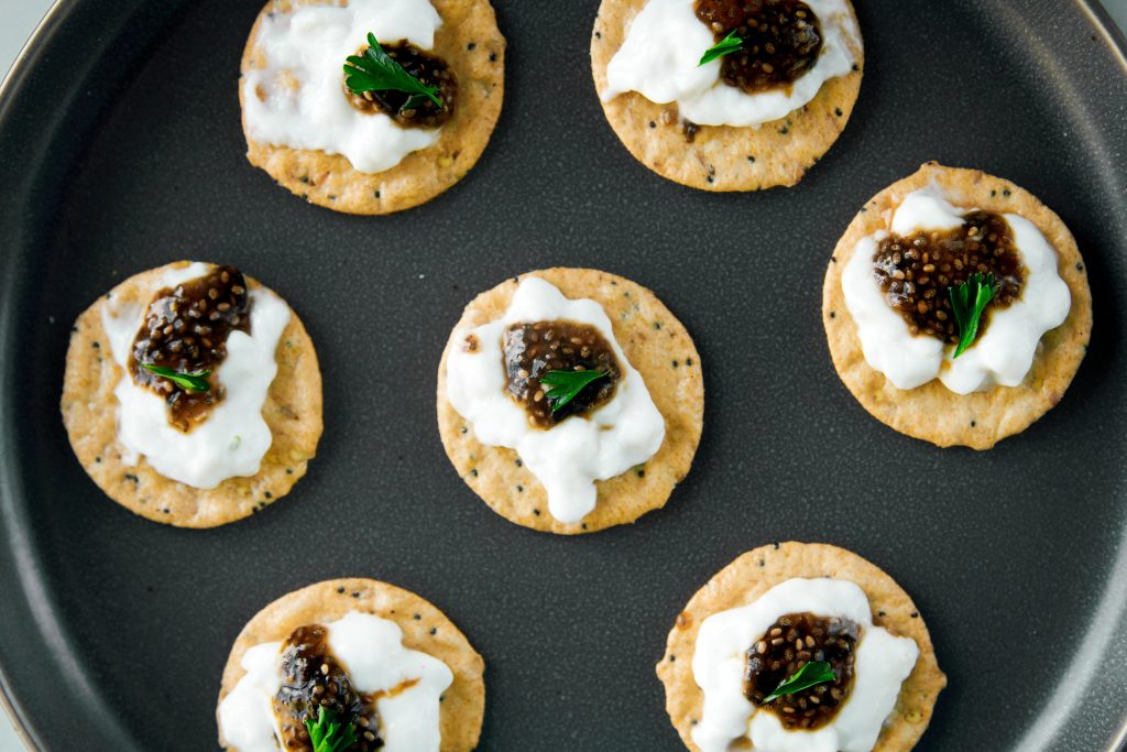 multiple crackers with sour cream and vegan caviar and herbs on them