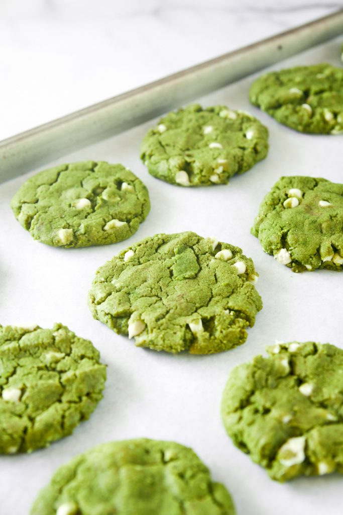 Rows of green matcha cookies with white chocolate chips on a baking sheet.