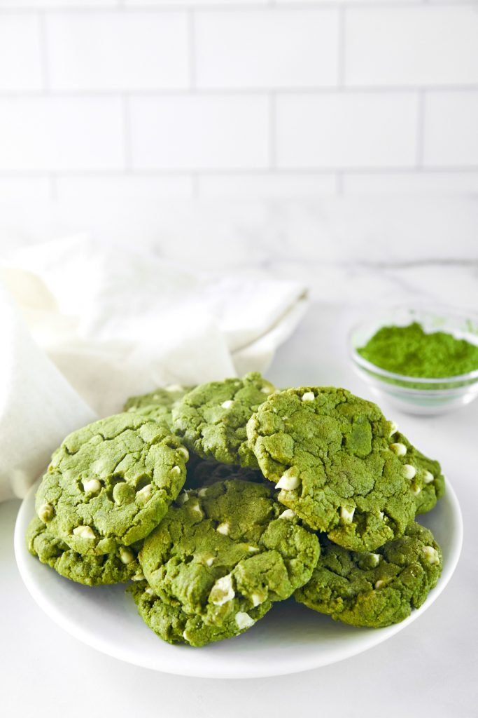  pile of vegan matcha cookies on serving plate with matcha in the background