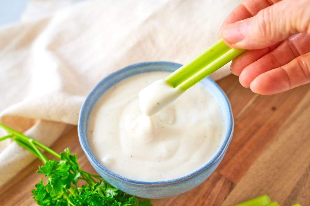 celery stalk being dipped into vegan ranch dressing
