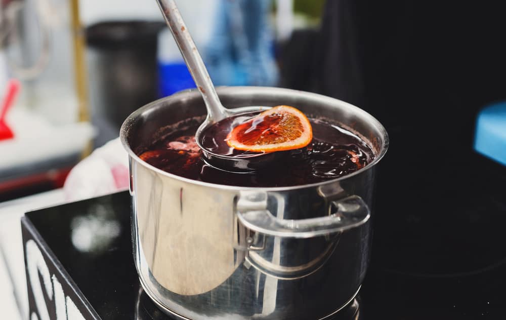 Ladle lifting slice of orange from a pot of mulled wine on the stove.