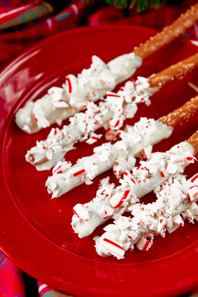 Christmas pretzel rods dipped in white chocolate and rolled in candy canes on a red plate