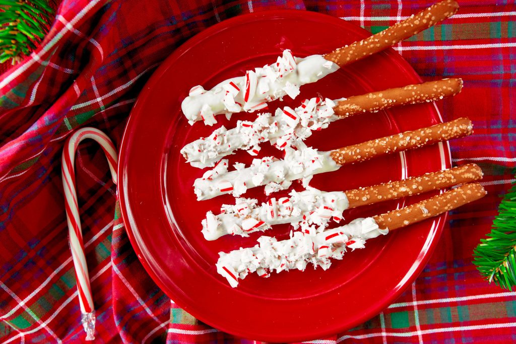 overhead shot of Christmas pretzel rods rolled in peppermint on a red plate on a tartan towel.