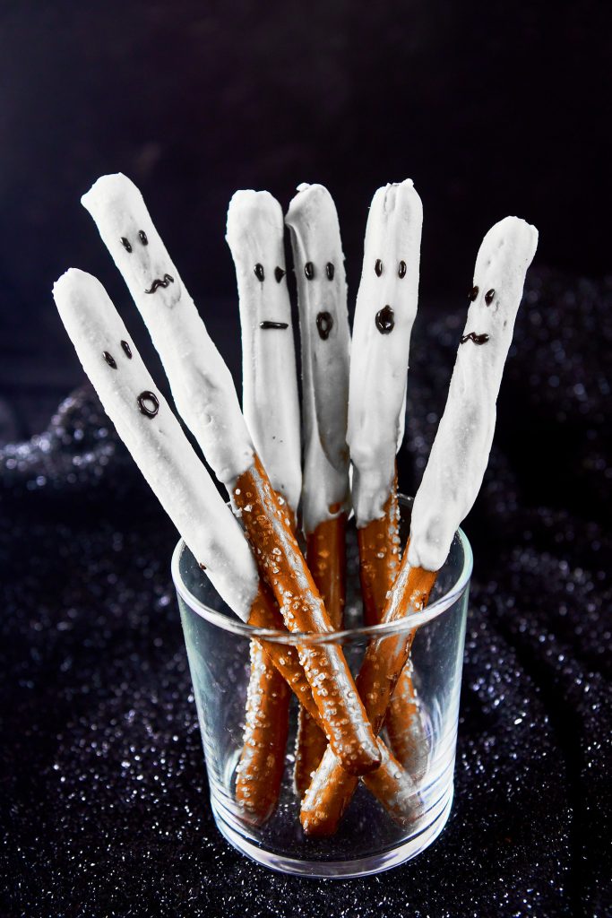 six ghost halloween pretzels in a glass container on a black background