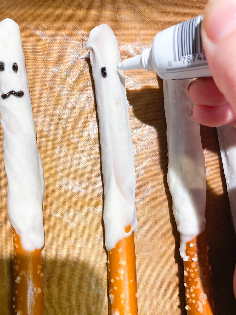 using icing to create a face on a pretzel rod that looks like a ghost