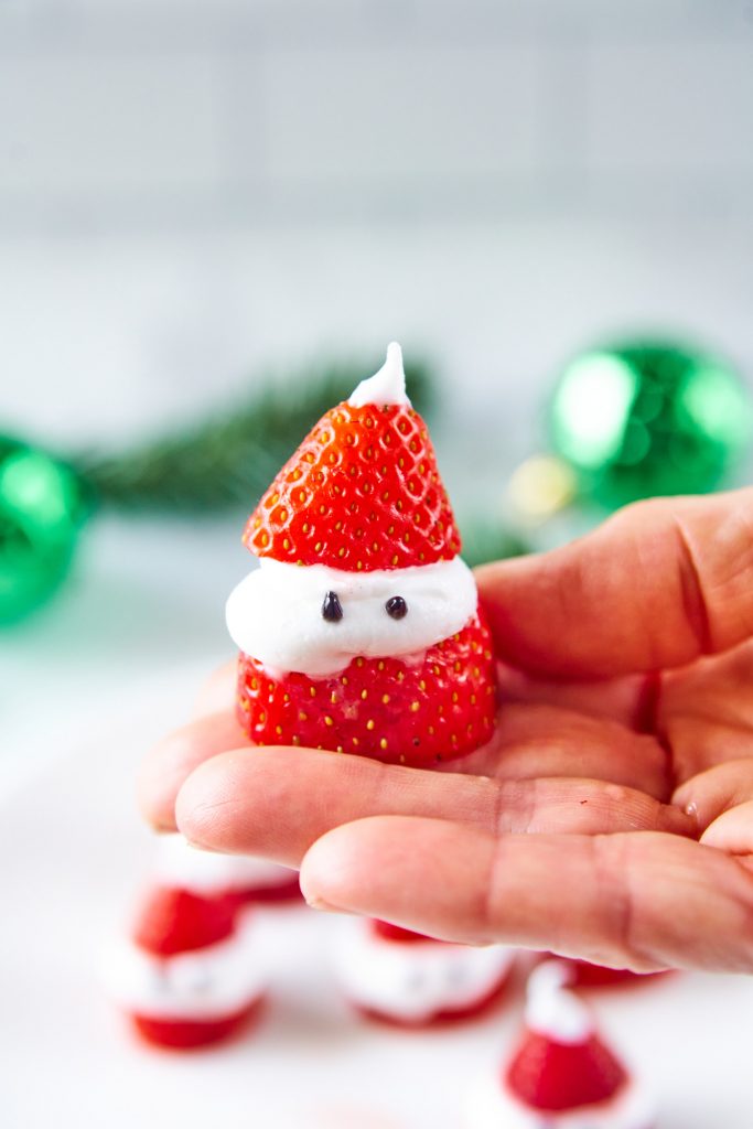 hand holding a homemade strawberry Santa Claus with green in the background