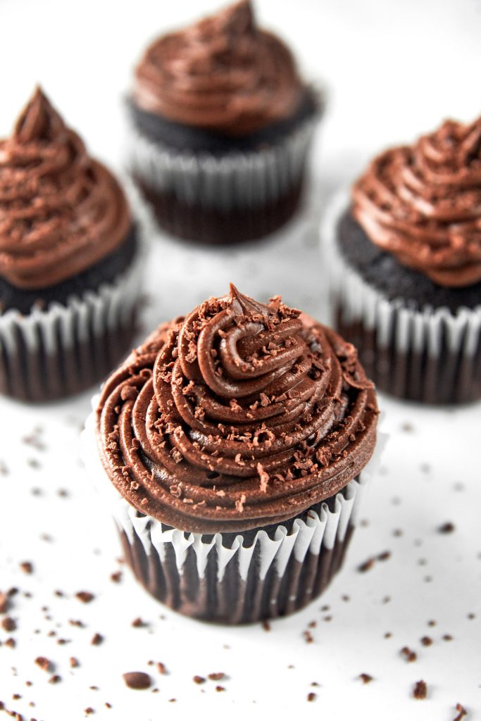 vegan chocolate cupcakes piled with frosting with chocolate shavings all around.