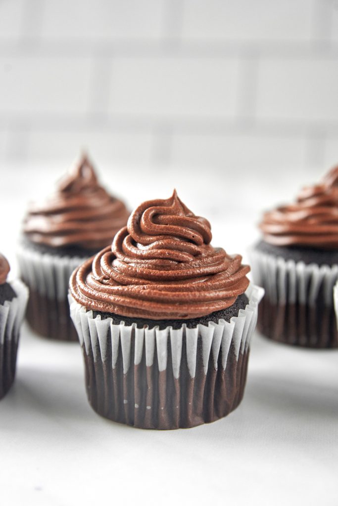 cupcakes being iced with vegan chocolate frosting