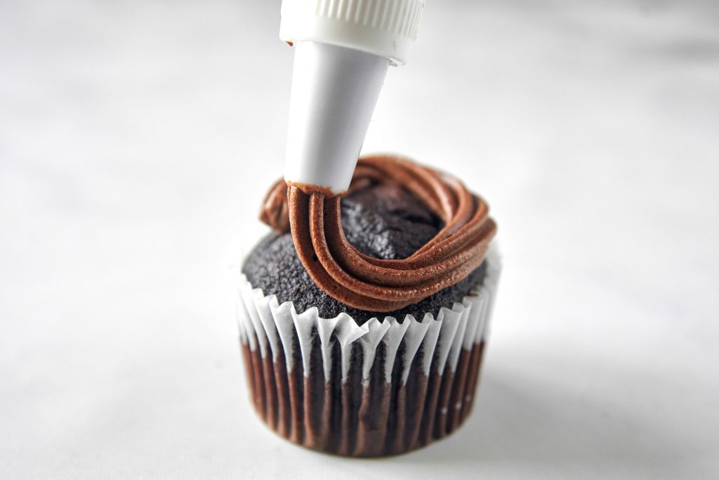 vegan chocolate frosting being piped onto a cupcake