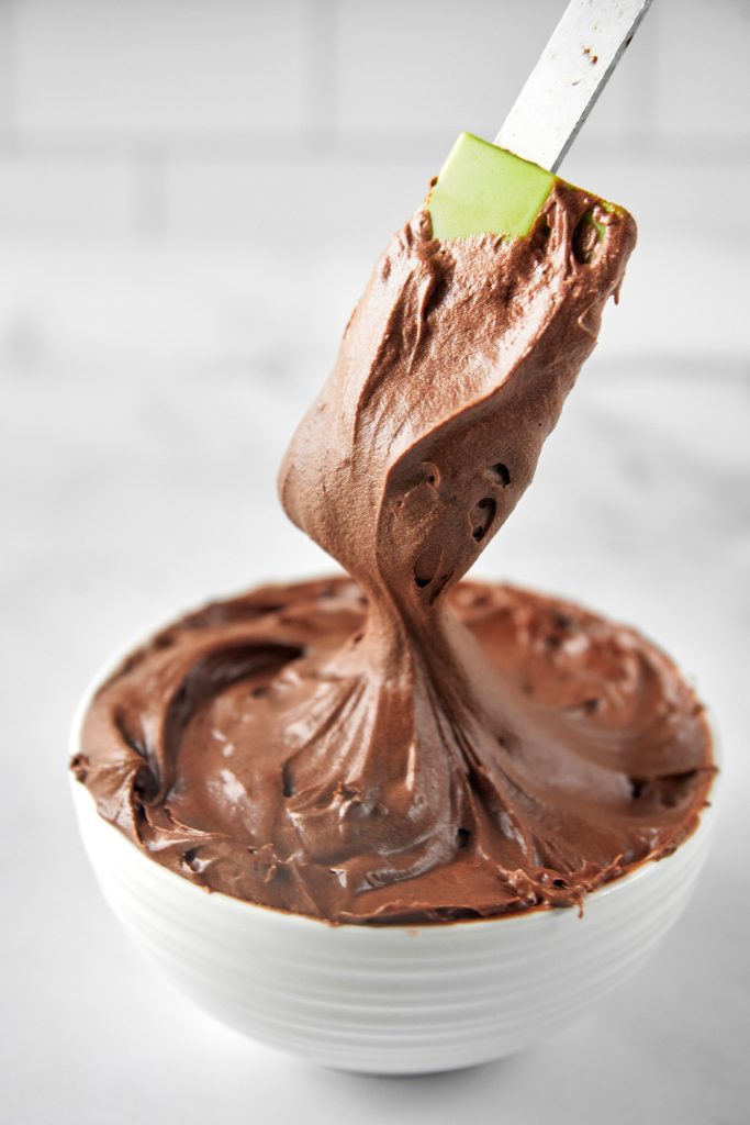 spatula scooping up vegan chocolate icing from a bowl
