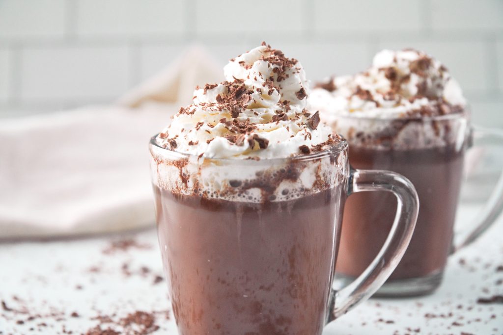 close up on two cups of vegan hot chocolate topped with chocolate shavings and vegan whipped cream